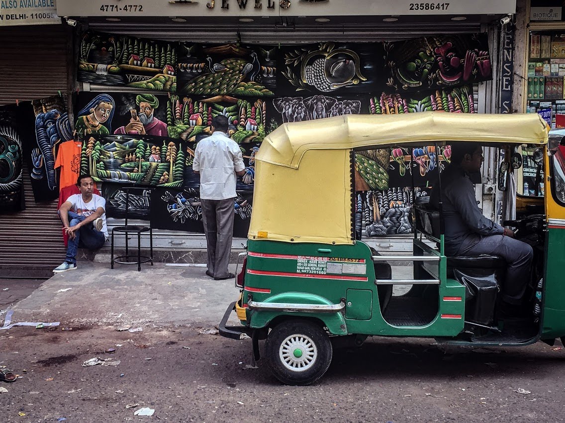 A green and yellow auto-rickshaw passing a painted storefront